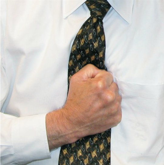 A man in a shirt and tie holding a clenched fist over his sternum.